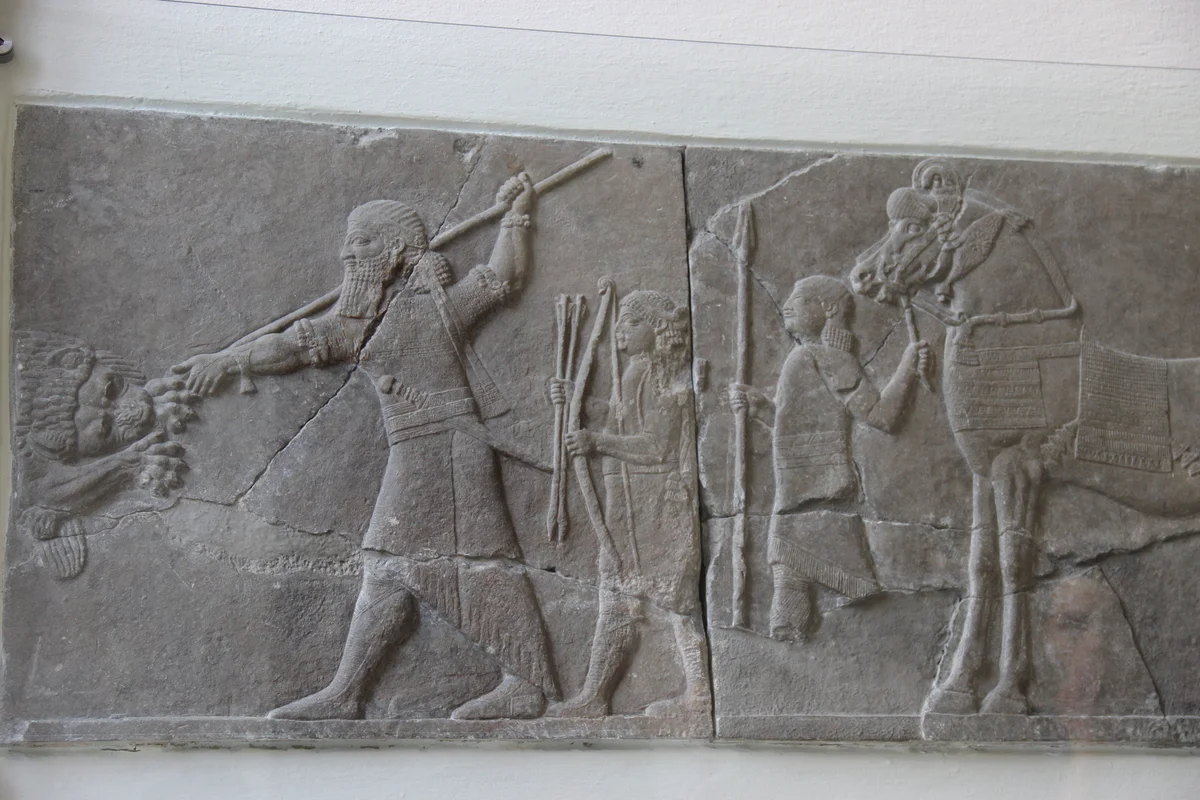 Kamienny relief przedstawiający króla z włócznią, lwa i towarzyszących królowi ludzi.